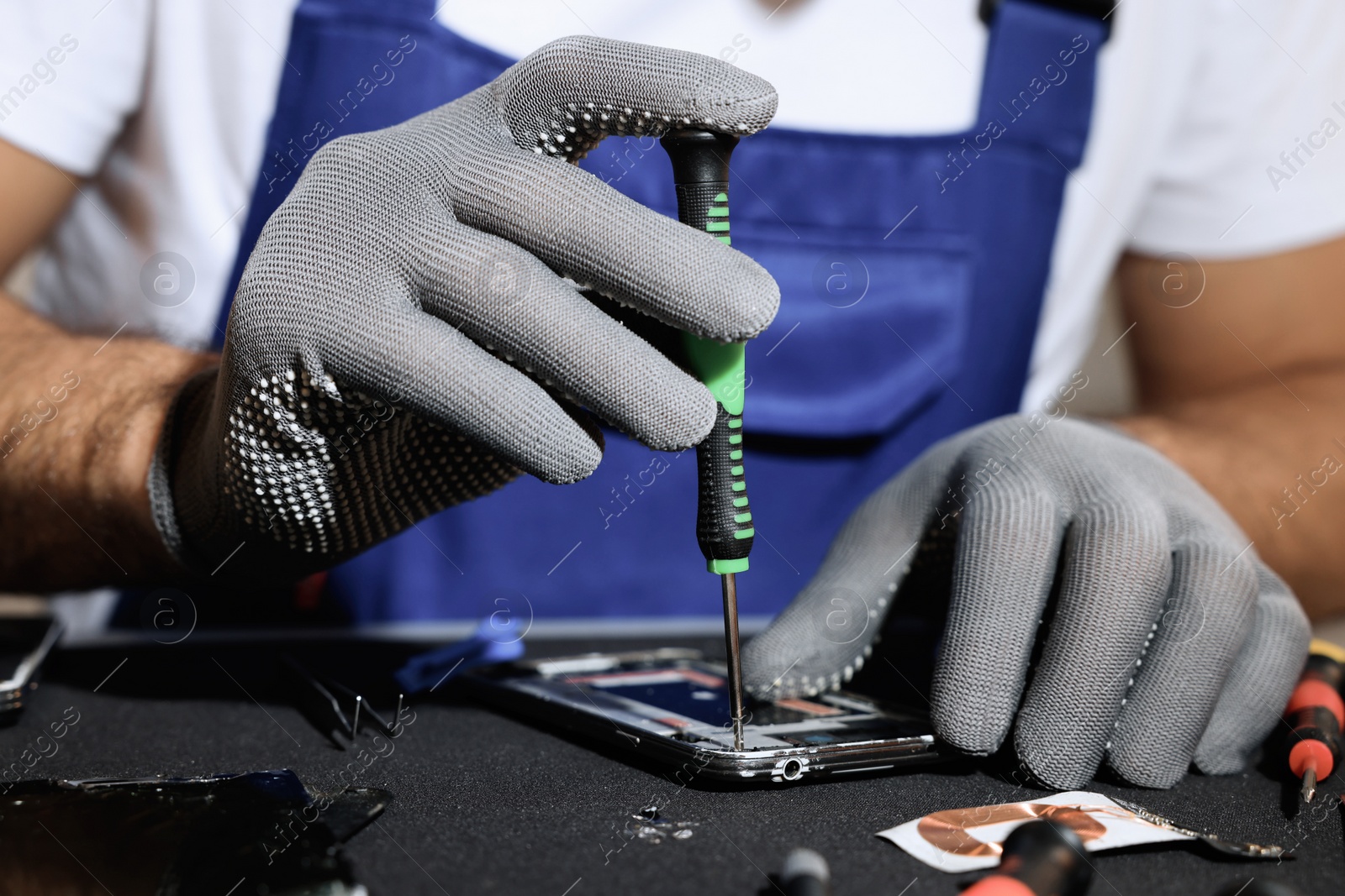 Photo of Technician repairing broken smartphone at table, closeup