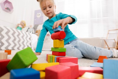 Photo of Cute little girl playing with colorful building blocks at home, focus on hand