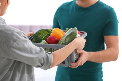 Photo of Courier giving plastic crate with products to customer at home, closeup. Food delivery service