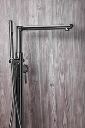 Photo of Modern bathtub faucet with hand shower on wooden background