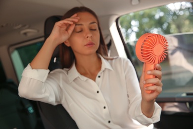 Photo of Young woman with portable fan suffering from heat in car on summer day