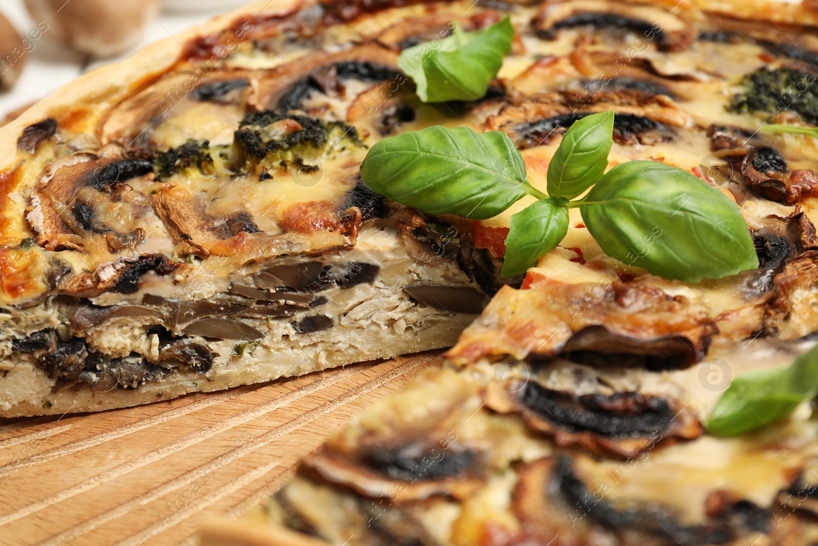 Photo of Delicious quiche with mushrooms and basil on wooden board, closeup