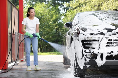 Photo of Happy woman covering automobile with foam at outdoor car wash