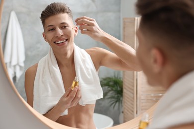 Photo of Handsome man applying serum onto his face in bathroom