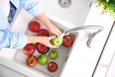 Photo of Woman washing fresh apples in kitchen sink, top view