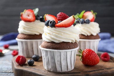 Photo of Sweet cupcakes with fresh berries on wooden board, closeup