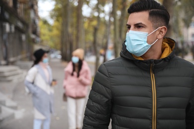 Photo of Man in medical face mask walking outdoors. Personal protection during COVID-19 pandemic