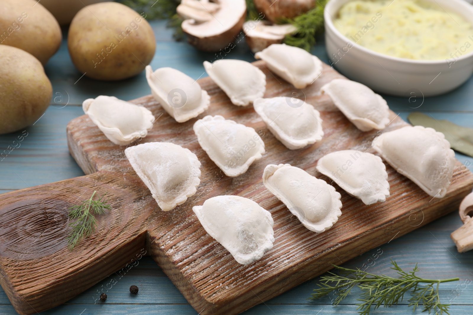 Photo of Raw dumplings (varenyky) and ingredients on light blue table