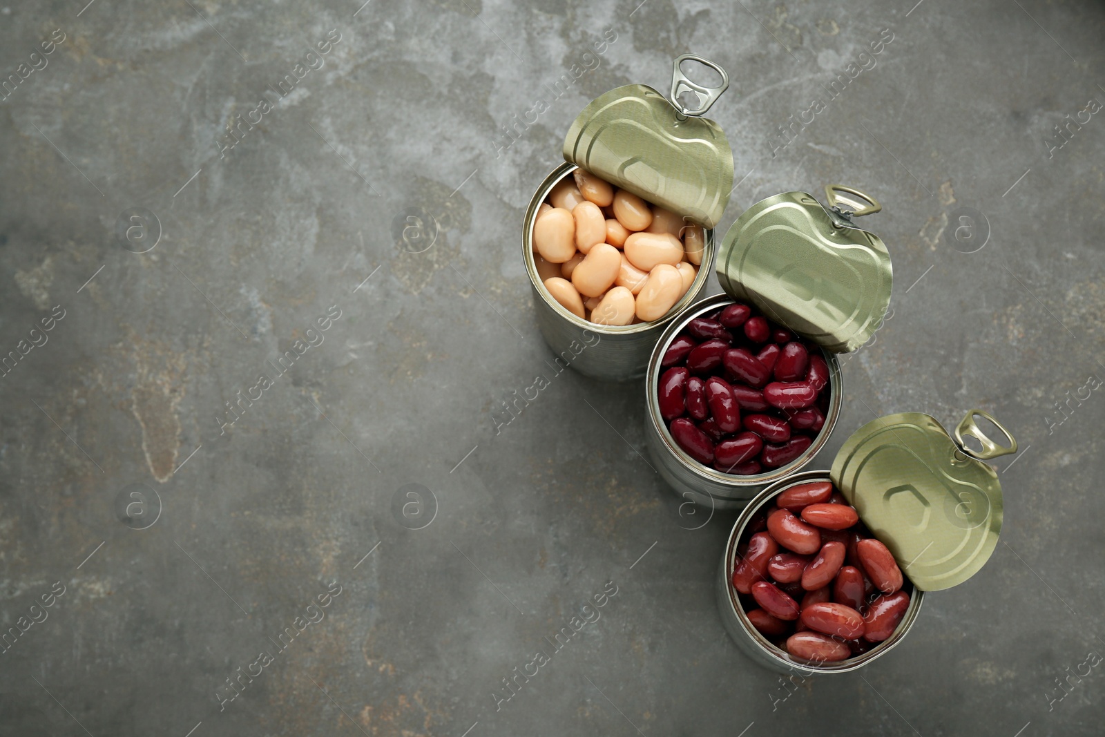 Photo of Tin cans with different canned kidney beans on grey table, flat lay. Space for text