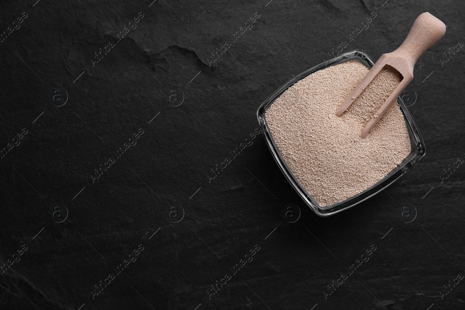 Photo of Bowl and scoop with active dry yeast on black table, top view. Space for text