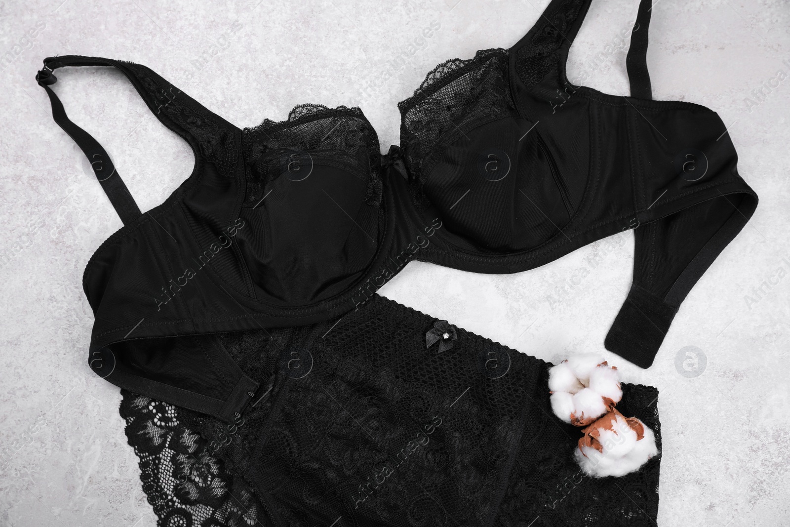 Photo of Elegant black plus size women's underwear and cotton flowers on light background, flat lay