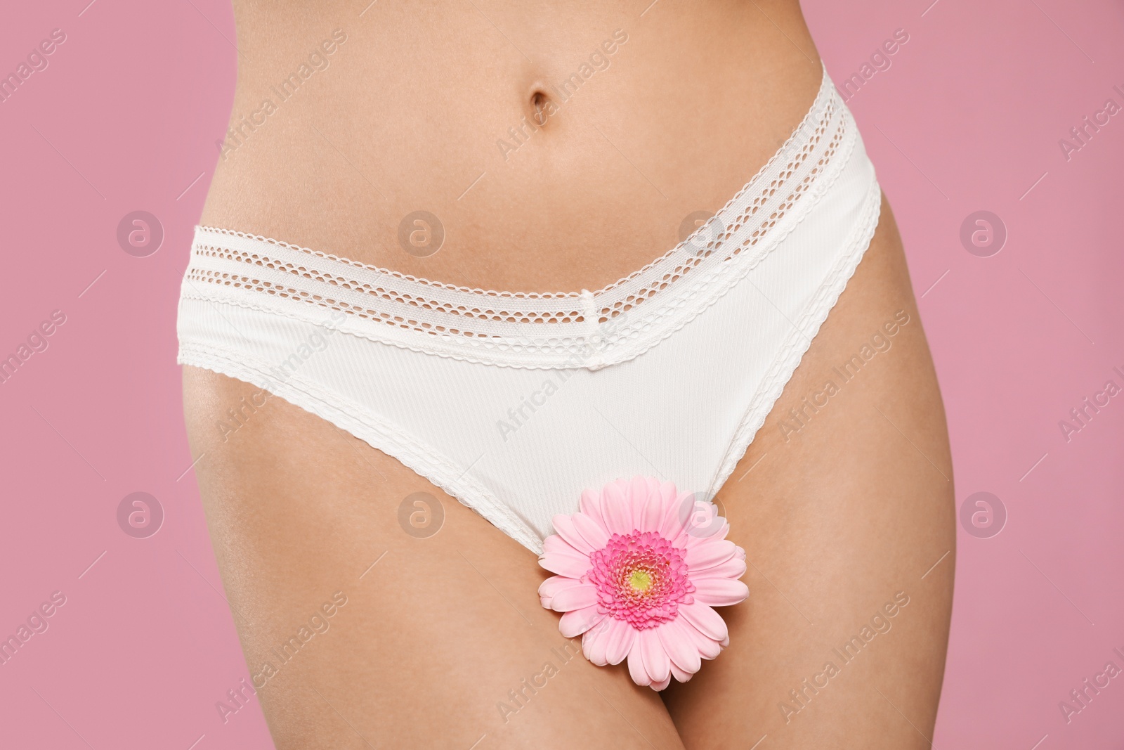 Photo of Woman in white panties with gerbera flower on pink background, closeup