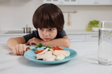 Photo of Cute little boy refusing to eat dinner in kitchen