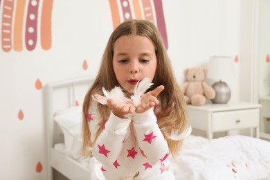 Photo of Cute little girl in pajamas playing with feathers at home. Happy childhood