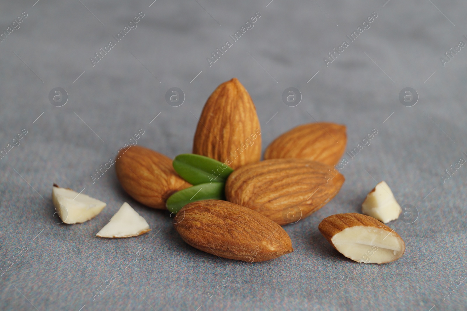 Photo of Delicious almonds and fresh leaves on grey table, closeup