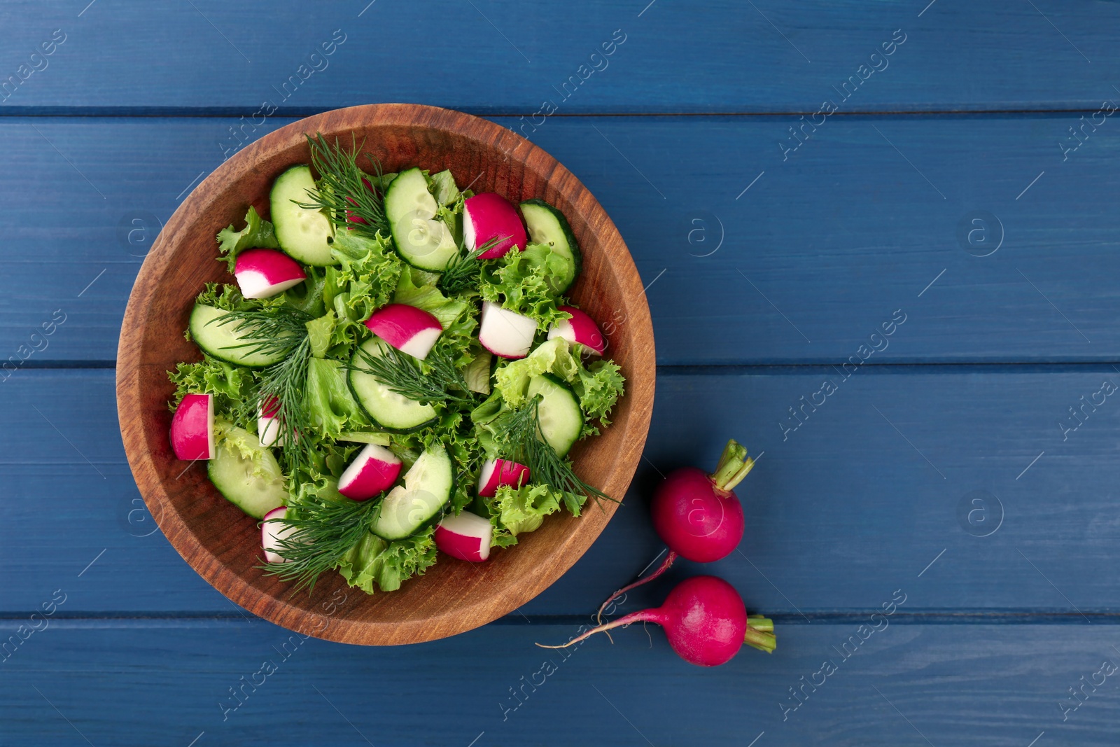 Photo of Delicious radish salad and ingredients on blue wooden table, top view. Space for text