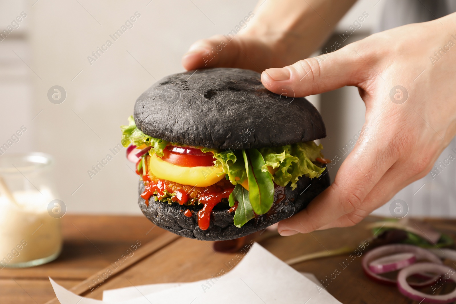 Photo of Woman holding tasty black vegetarian burger over table, closeup