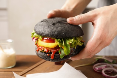 Woman holding tasty black vegetarian burger over table, closeup