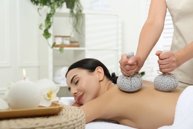 Young woman receiving herbal bag massage in spa salon