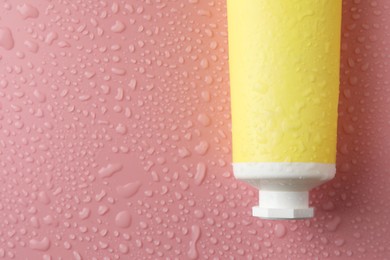 Moisturizing cream in tube on pink background with water drops, top view. Space for text