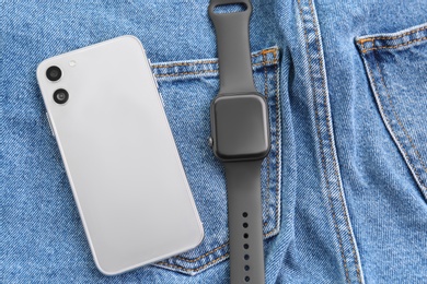Photo of Stylish smart watch and phone on jeans, flat lay