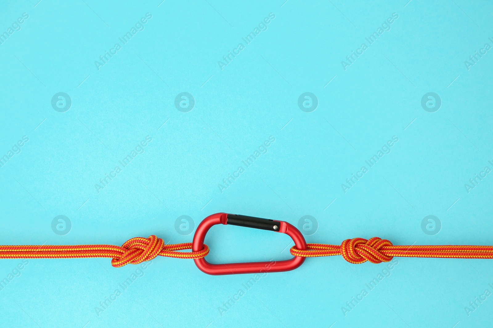 Photo of One metal carabiner with ropes on light blue background, top view. Space for text