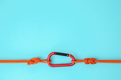 Photo of One metal carabiner with ropes on light blue background, top view. Space for text