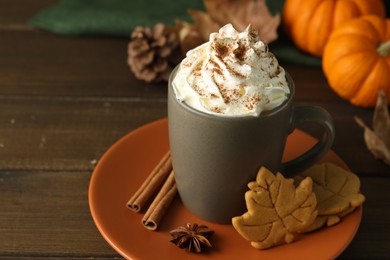 Photo of Tasty pumpkin spice latte with whipped cream in cup and cookies on wooden table, closeup