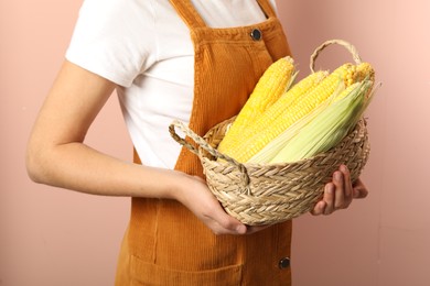 Woman with basket of corn cobs on coral background, closeup