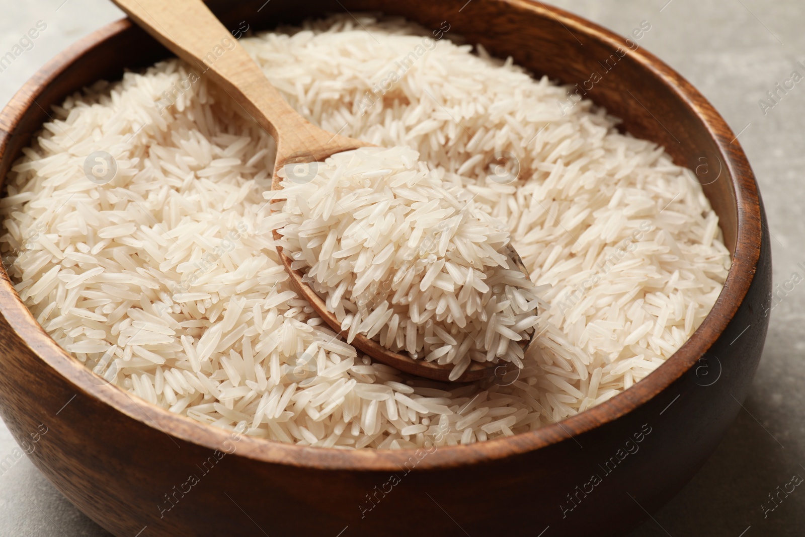 Photo of Raw basmati rice in bowl and spoon on table, closeup