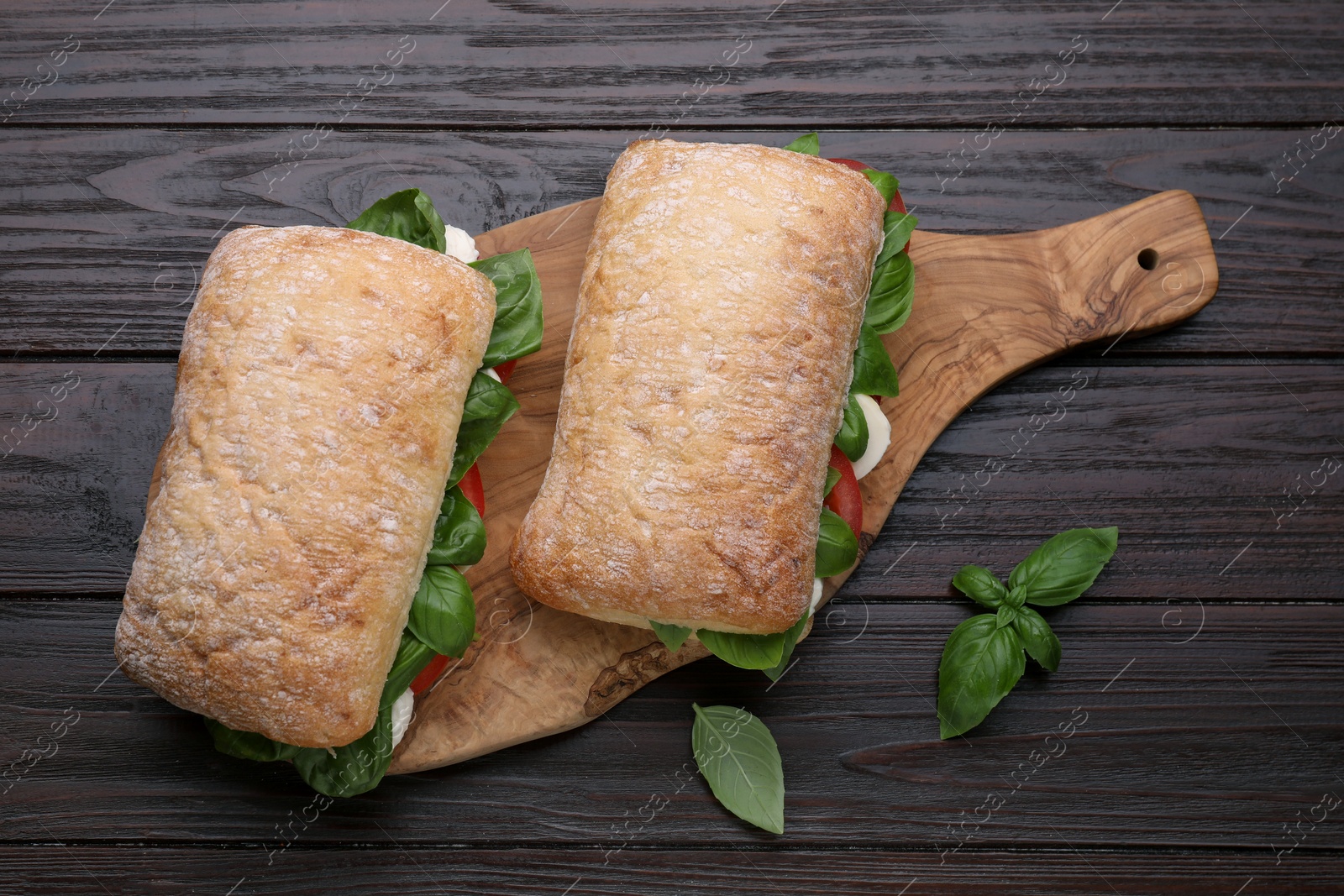 Photo of Delicious Caprese sandwiches with mozzarella, tomatoes and basil on wooden table, flat lay