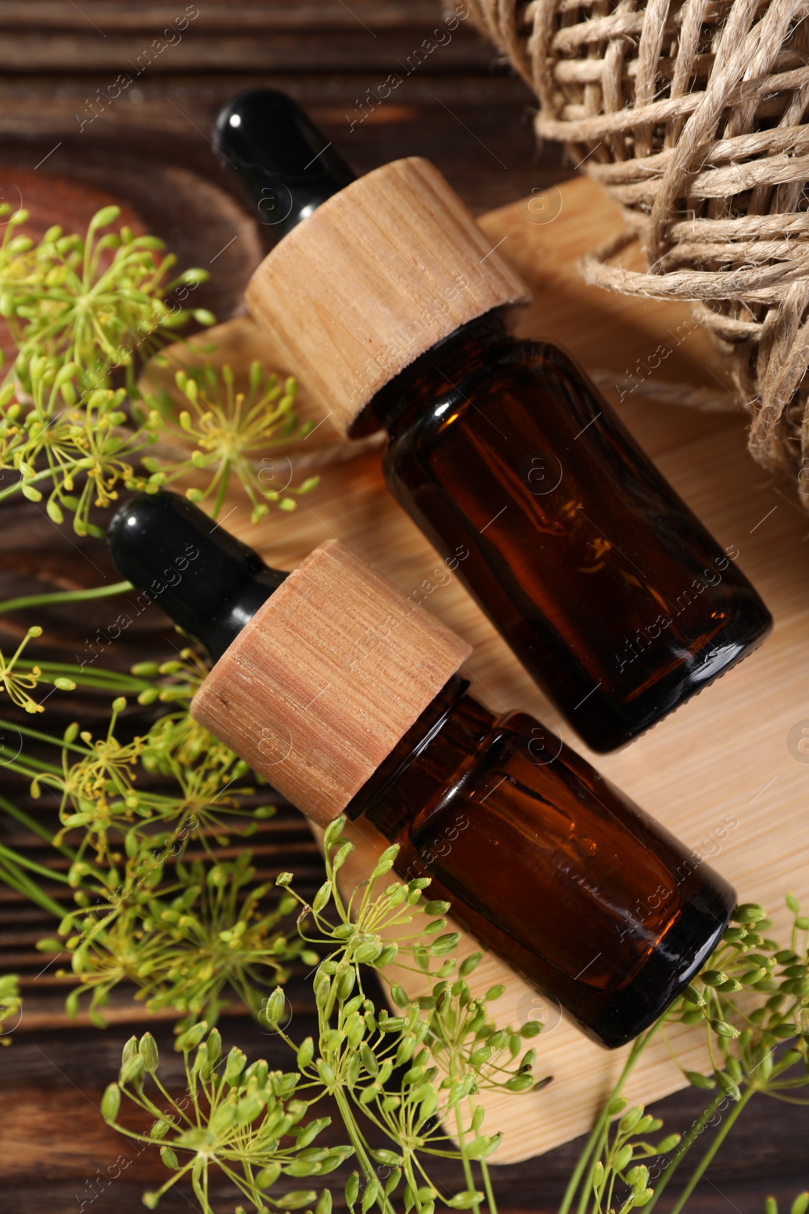 Photo of Bottle of essential oil, fresh dill and twine on wooden table, flat lay