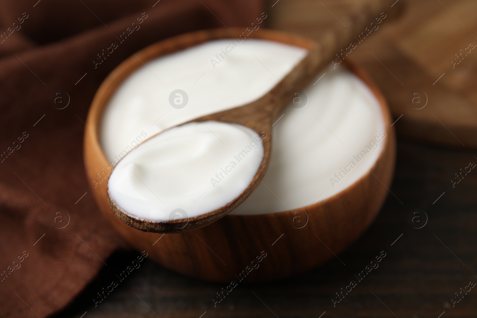 Photo of Delicious natural yogurt in bowl and spoon on wooden table, closeup