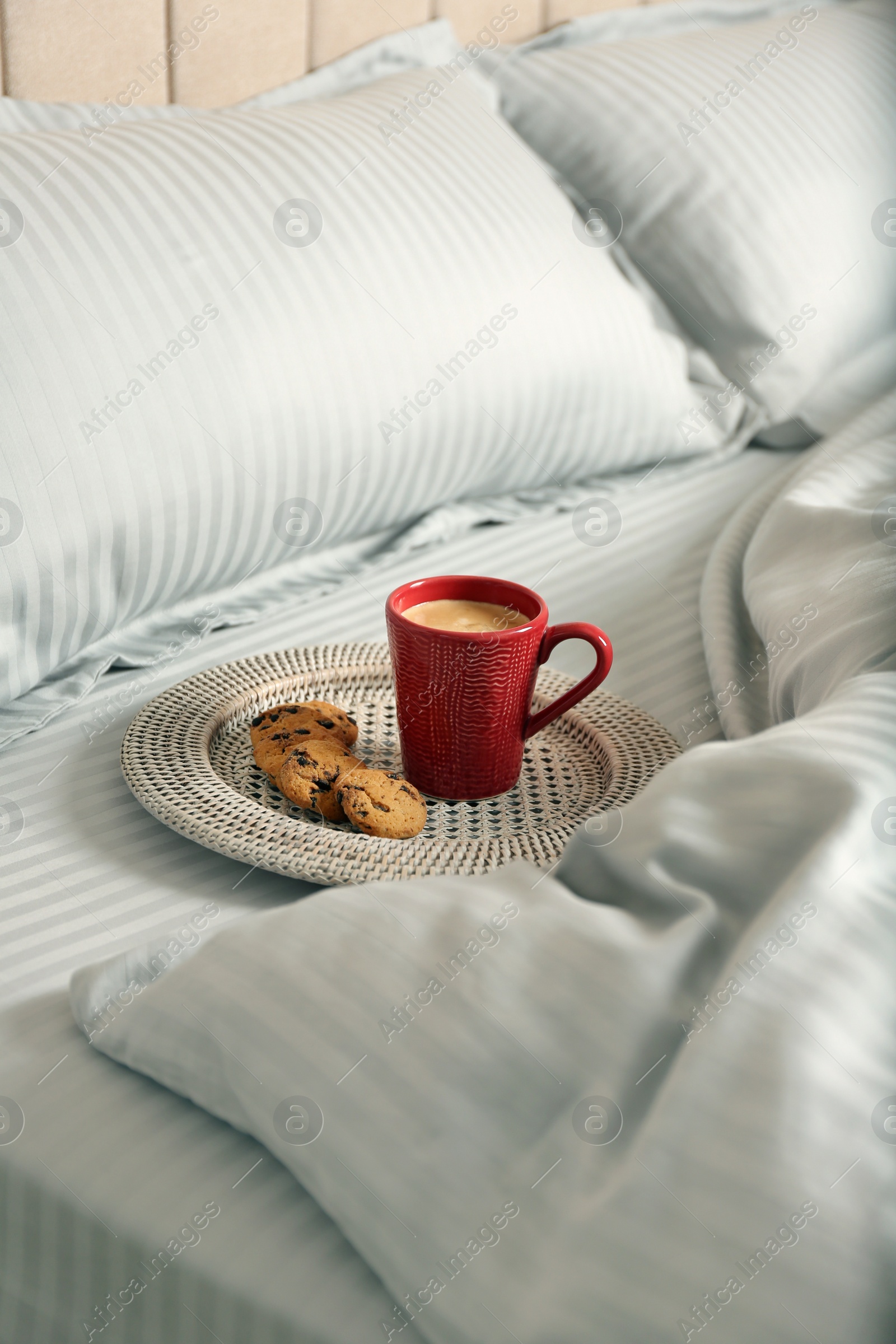 Photo of Cup of aromatic coffee and cookies on bed with soft blanket