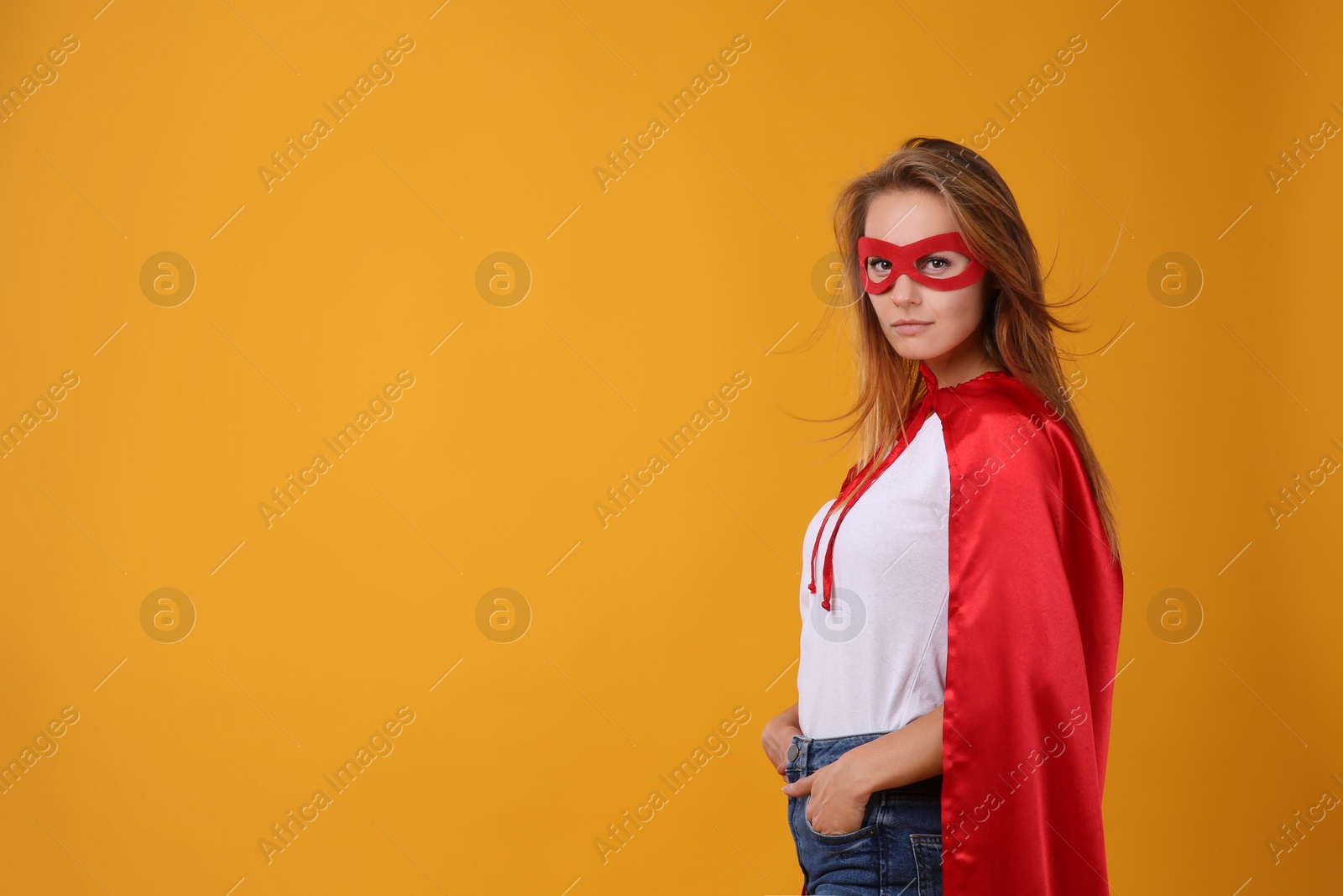 Photo of Confident woman wearing superhero cape and mask on yellow background. Space for text