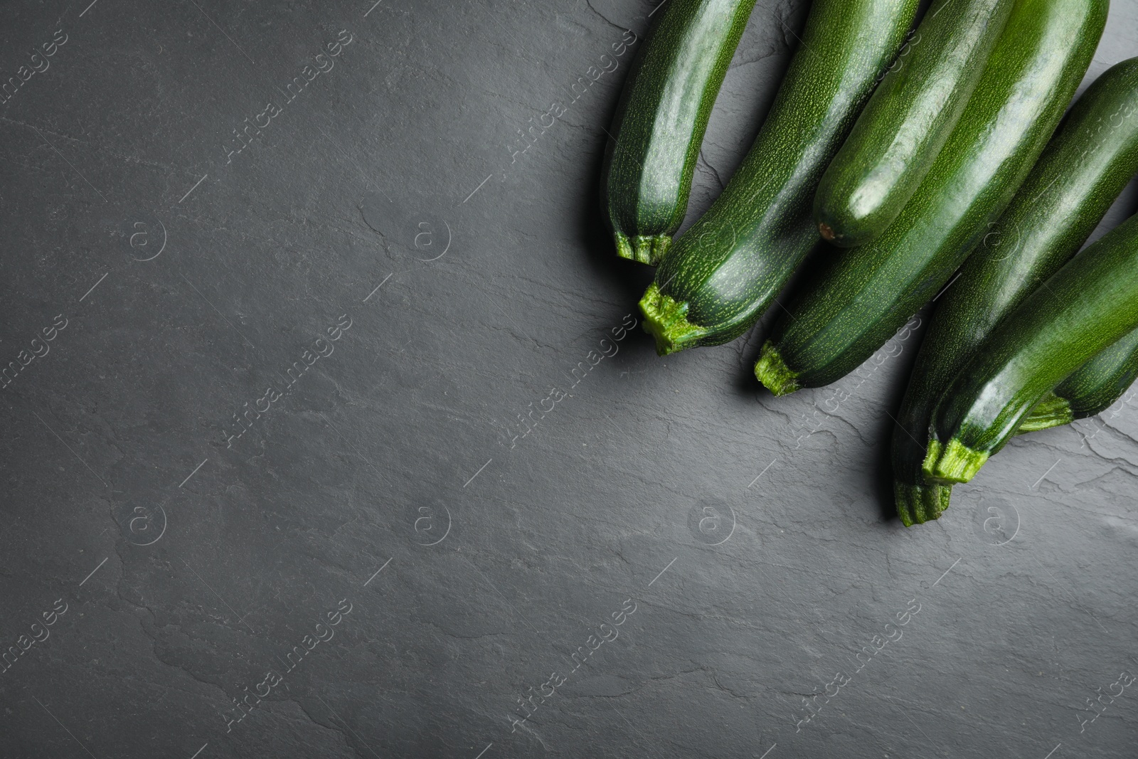 Photo of Green ripe zucchinis on black slate table, flat lay. Space for text