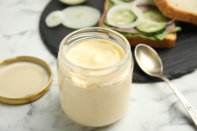 Jar of delicious mayonnaise near fresh sandwich on white marble table