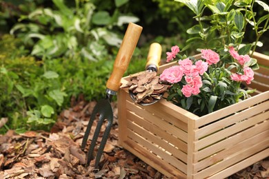 Photo of Bark chips, wooden box with flowers, gloves, fork and trowel in garden. Space for text