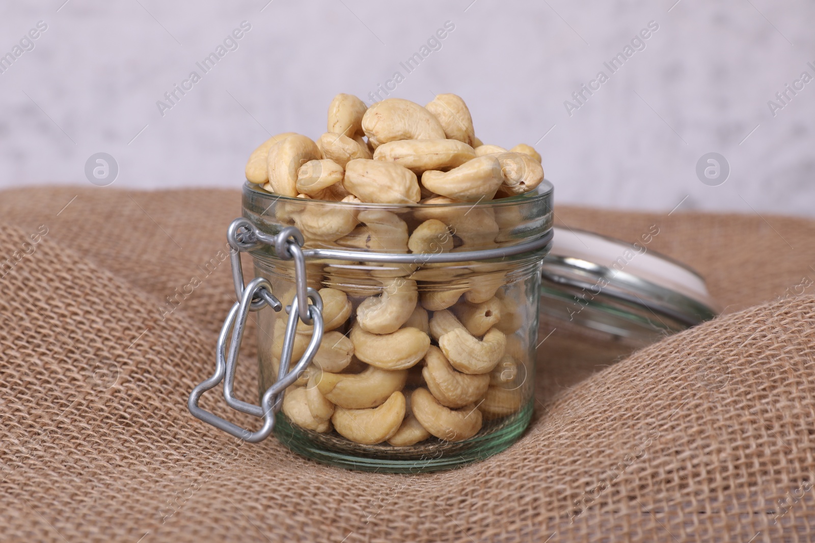 Photo of Tasty cashew nuts in glass jar on light brown fabric, closeup