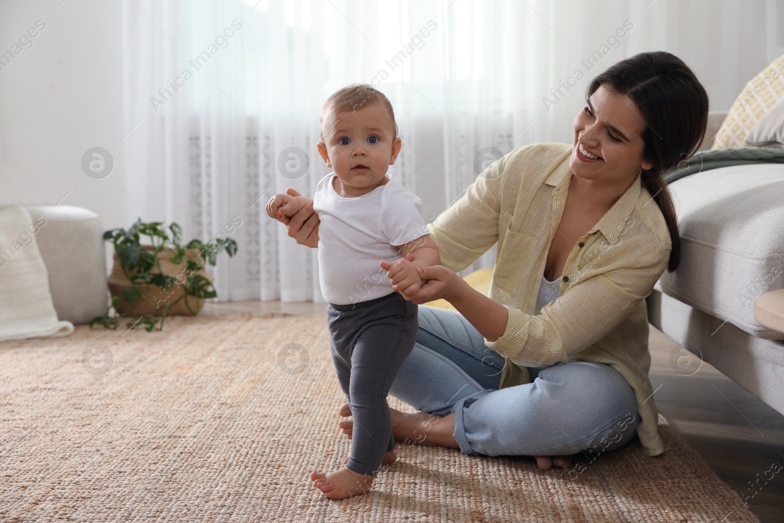 Photo of Mother supporting her baby daughter while she learning to walk at home