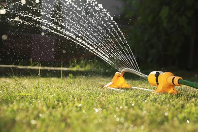 Photo of Automatic sprinkler watering green grass on sunny day in garden. Irrigation system