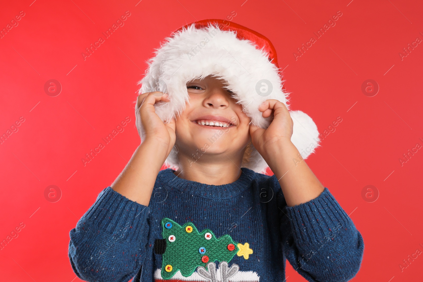 Photo of Happy little child in Santa hat on red background. Christmas celebration