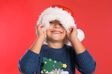 Photo of Happy little child in Santa hat on red background. Christmas celebration