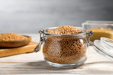 Photo of Mustard seeds in glass jar on white wooden table, closeup