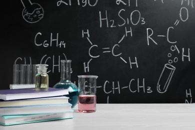 Photo of Laboratory glassware and school supplies on table against blackboard with chemical formulas