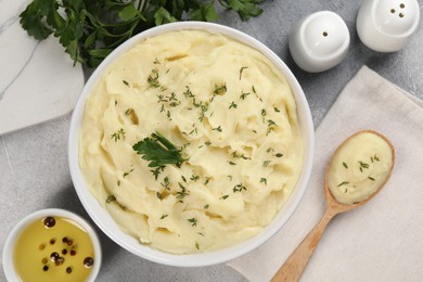 Photo of Bowl of tasty mashed potato, parsley, olive oil and pepper on grey marble table, flat lay