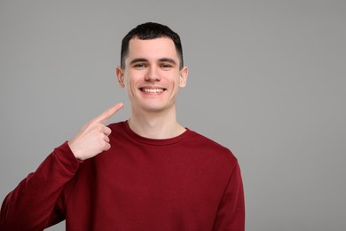 Photo of Handsome young man showing his clean teeth on grey background, space for text