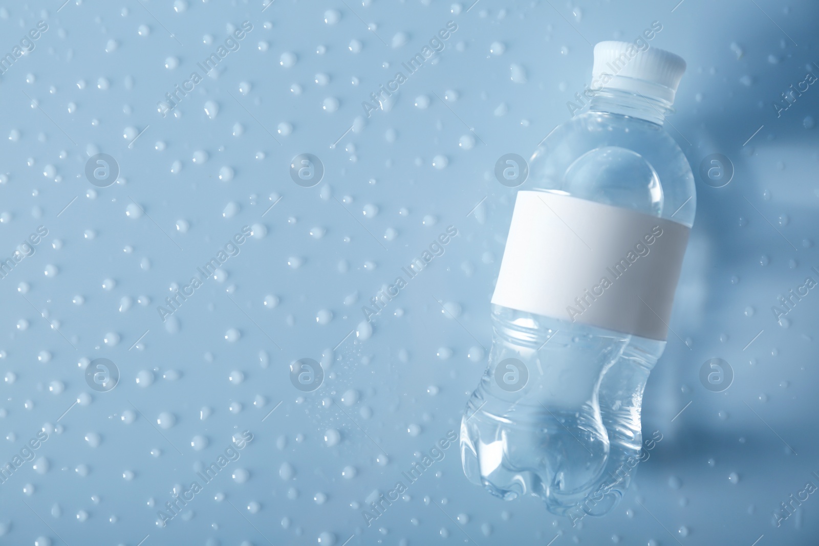 Photo of Bottle of water on wet light surface, top view. Space for text