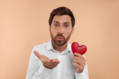 Photo of Man holding red heart and blowing kiss on beige background