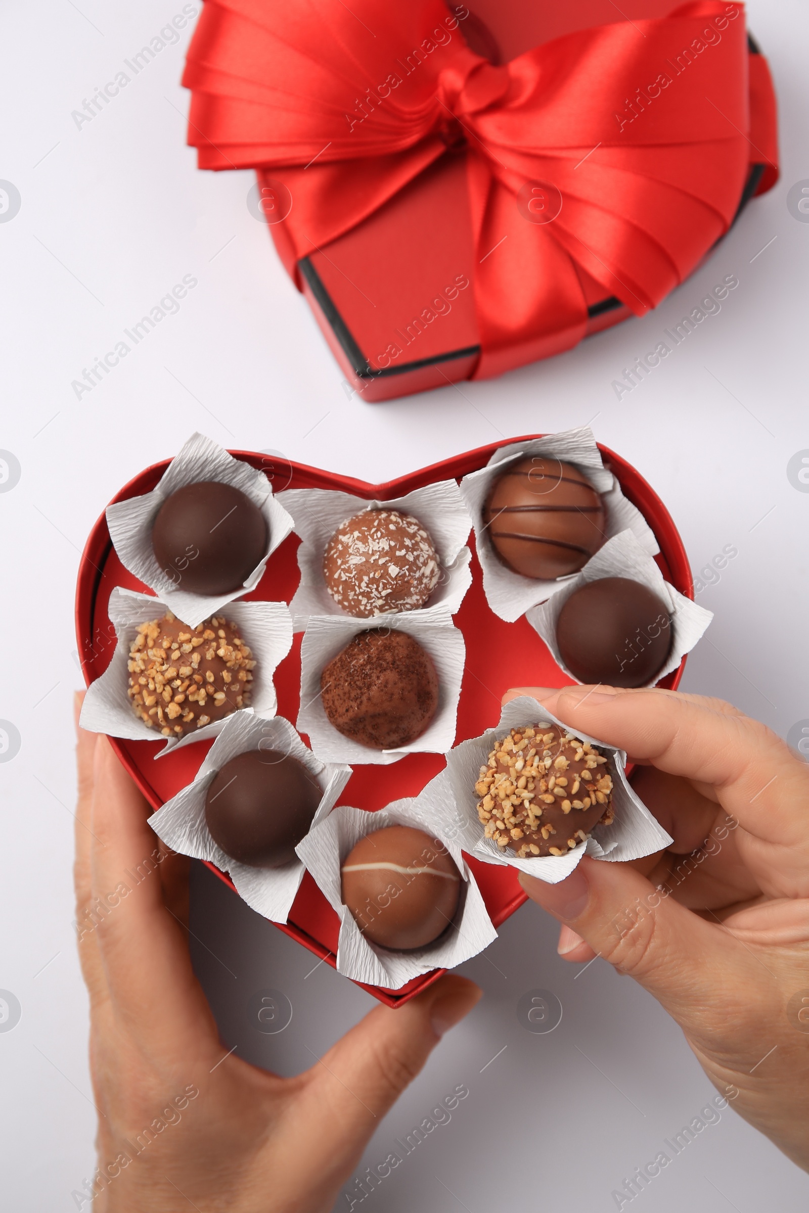 Photo of Woman taking delicious chocolate candy from heart shaped box on white background, top view